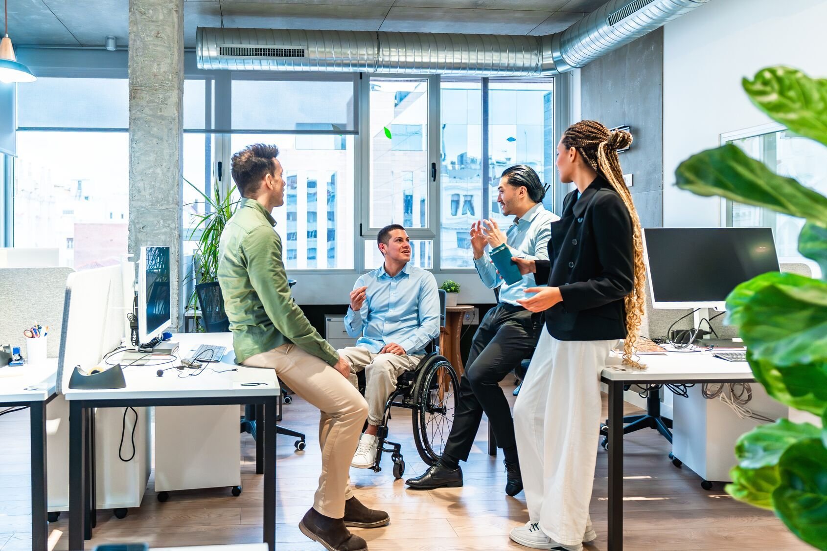 Web_Wide - Zróżnicowany zespół biznesowy omawiający projekt w nowoczesnym biurze z niepełnosprawnym kolegą na wózku inwalidzkim